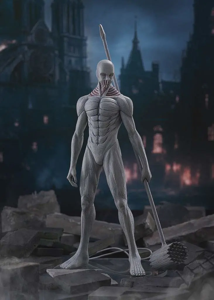 Attack on Titan Armored Titan statue in a detailed, muscular pose, holding a spear and standing on a base with a broom, set against a dark, ruined cityscape background.