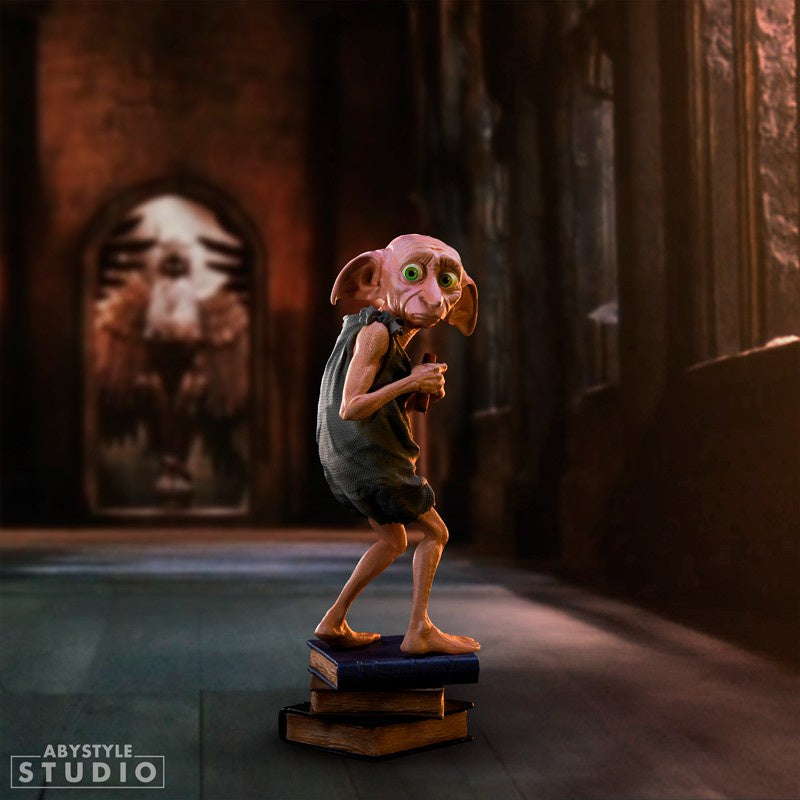 A PVC figurine of Dobby the House-Elf from Harry Potter, standing on a stack of books in a dimly lit room.