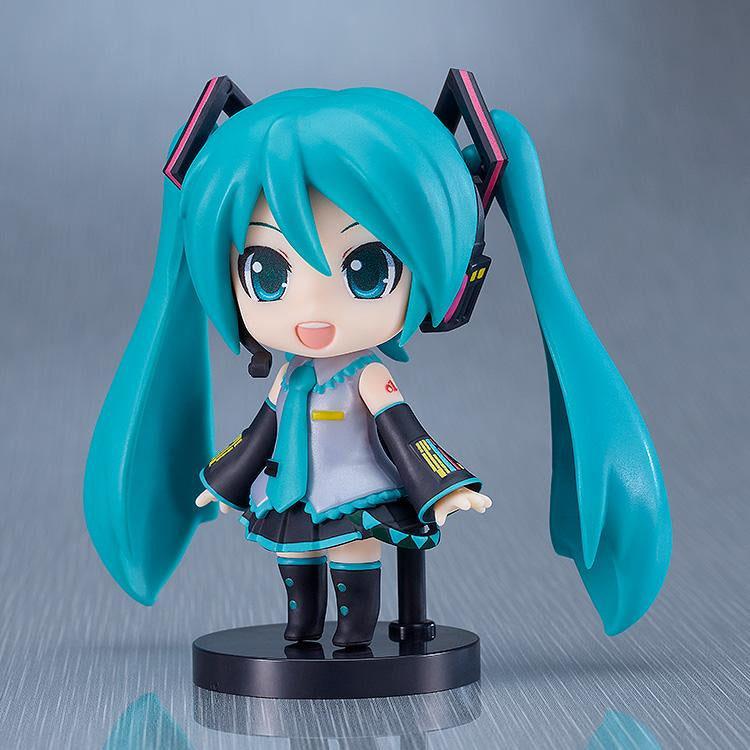 A Chibi Hatsune Miku in her classic outfit, blue tie, grey shirt and black skirt with neon blue rims on the end of the skirt. Bright neon blue hair and black headphones with pinks details