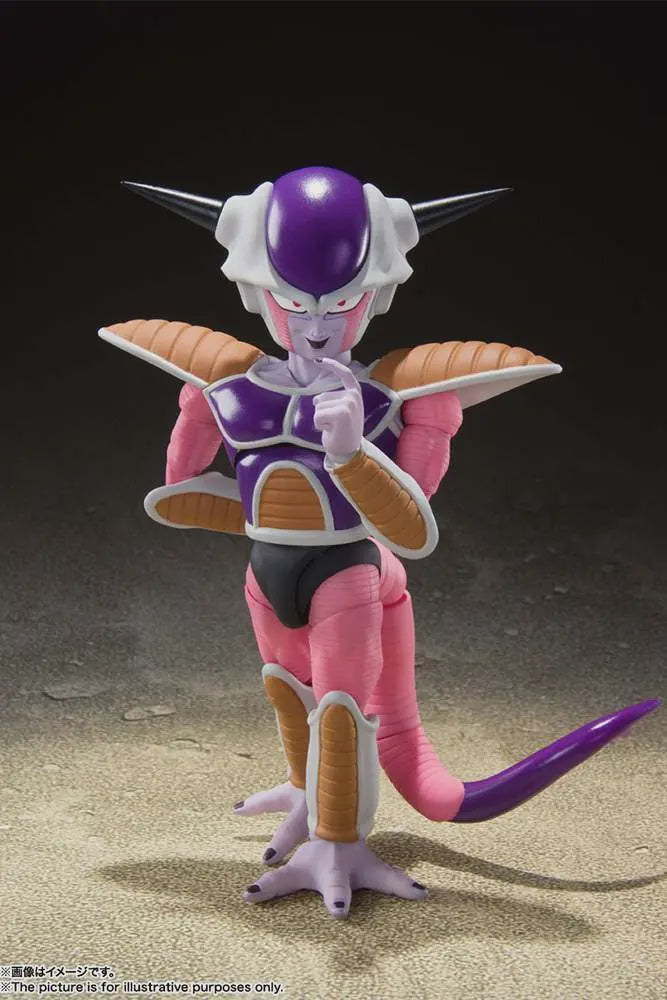 A collectible action figure of Frieza from Dragon Ball Z, posed standing on a sandy surface against a dark studio background. The figure features pink skin, a purple chest and tail, white horns and collar, and gold armor accents.