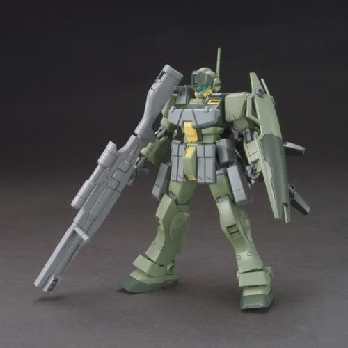 A painted model robot/mecha figure in muted olive green, gray, and small yellow accents, posed holding a large gray rifle with a shield on its back against a dark studio background.