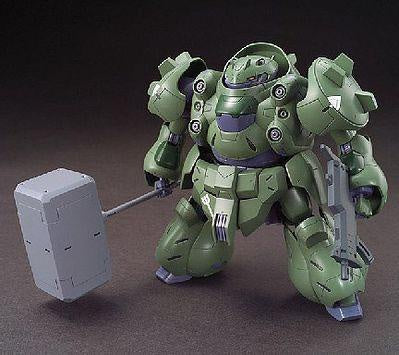 A green mecha robot action figure holding a large gray hammer in one hand and a rifle in the other, posed against a dark brown studio background.