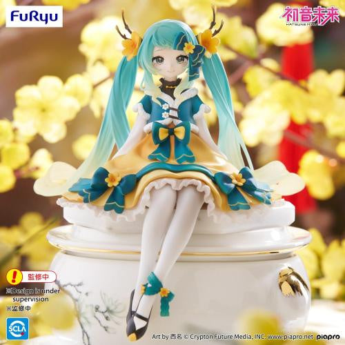 Figurine of a character with teal hair and a blue dress sitting on a pedestal with flowers in the background.