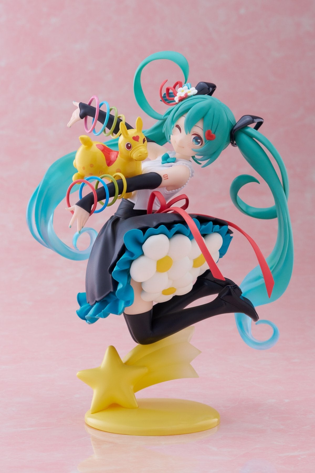 Colorful figurine with teal hair and black outfit on a pink background