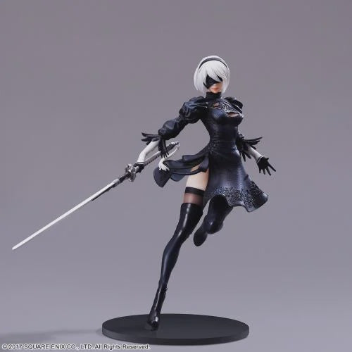 A detailed anime figurine of 2B from NeuroArchitects, posed dynamically while holding a sword. The figure features short white hair, a black eye mask, a black dress, thigh-high black stockings, and stands on a round black base against a neutral gray background.