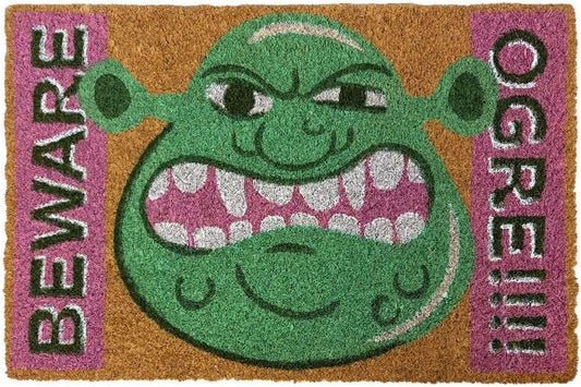A rectangular coir doormat featuring a large green cartoon monster face with an open mouth showing pink and white teeth, bordered by pink sections with the words 'BEWARE' on the left and 'OGREIII' on the right.